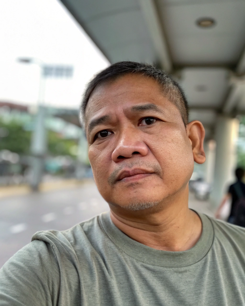 AI generated image by Red Panda AI: selfie portrait taken on iphone. thai middle-aged man, neutral expression, looking straight at the camera, both ears clearly visible, short hair, bright sclera, clear black eyes, semi-blurry, phone shot of low quality, tshirt