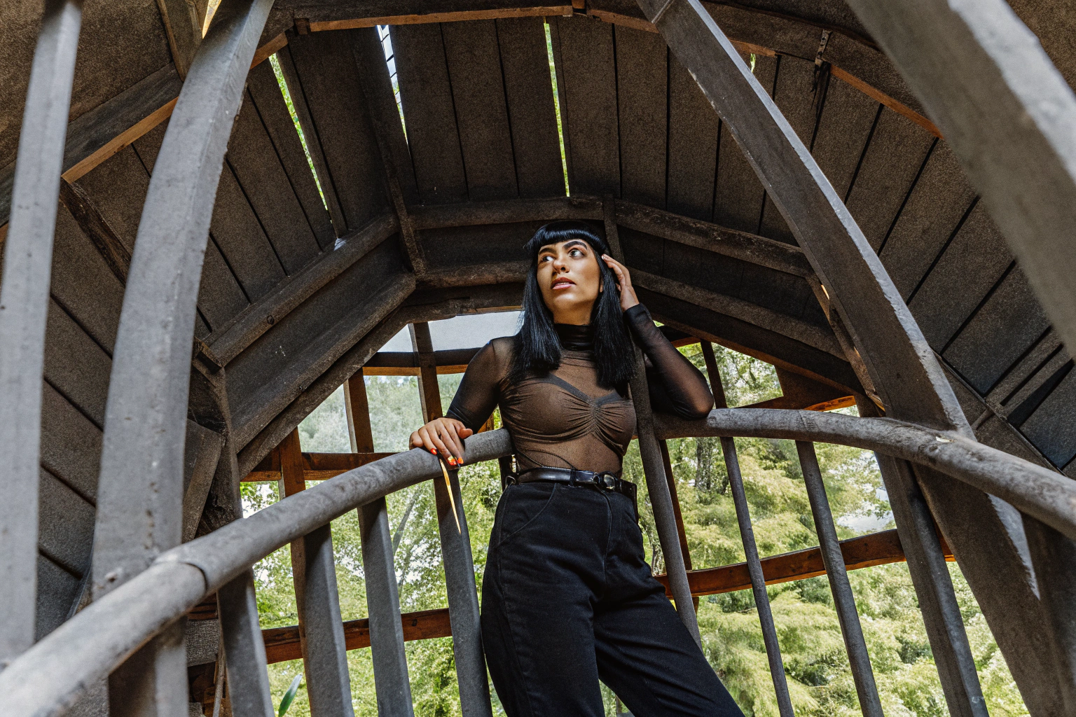 AI generated image by Red Panda AI: fisheye, beautiful woman, black bangs, collar, scared look, crop tight longsleeve sheer t-shirt and extra_large baggy black pants, standing on a tower over a fantasy forest
