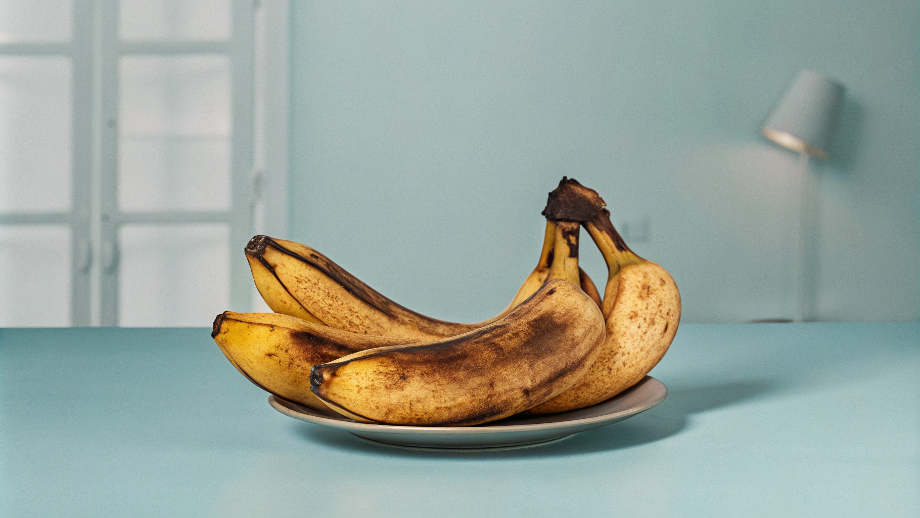 AI generated image by Red Panda AI: A dreamlike scene in a muted, nostalgic color palette, where several, overripe brown banana are lying on a child's plate. The bananas appear strange and exotic and unknown and very distorted, with an almost mythical aura, symbolizing scarcity and unfamiliarity. In the background, only vague, hint at a very old Soviet kitchen—faint outlines of a cupboard, a dim lamp, and shadows that evoke feelings of care, hesitation, and pressure. The scene is blurred around the edges, creating a sense of fading memory, with a melancholic and surreal atmosphere, evoking both love and reluctance. The kitchen is cluttered