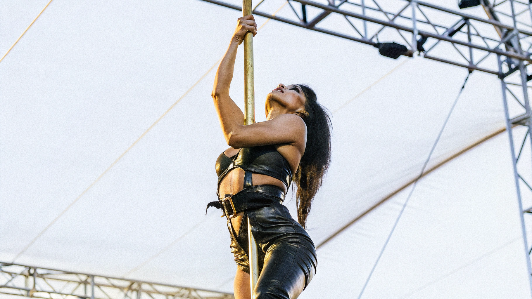 AI generated image by Red Panda AI: "A stunning woman, dressed in a tight black leather outfit, performs an impressive pole dance on stage during a rock concert. The focus is only on her, with no other people visible. She moves with strength, elegance, and sensuality, illuminated by dramatic red and blue stage lights. Hyper-realistic style, cinematic focus, energetic and vibrant atmosphere, 4K quality."