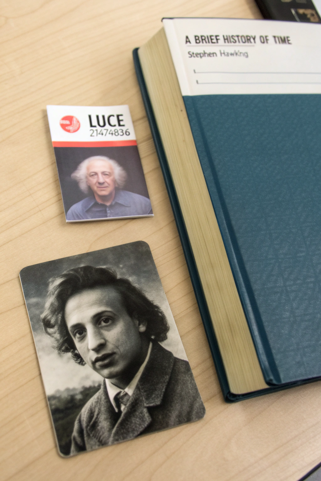 AI generated image by Red Panda AI: A table with three distinct items placed in an organized manner. On the left side, a student ID card is visible, showing the student's name Luce and the ID number 21474836. Next to the card, there is a copy of the book A Brief History of Time by Stephen Hawking. On the top of the book, black-and-white photo of Albert Einstein is placed.
