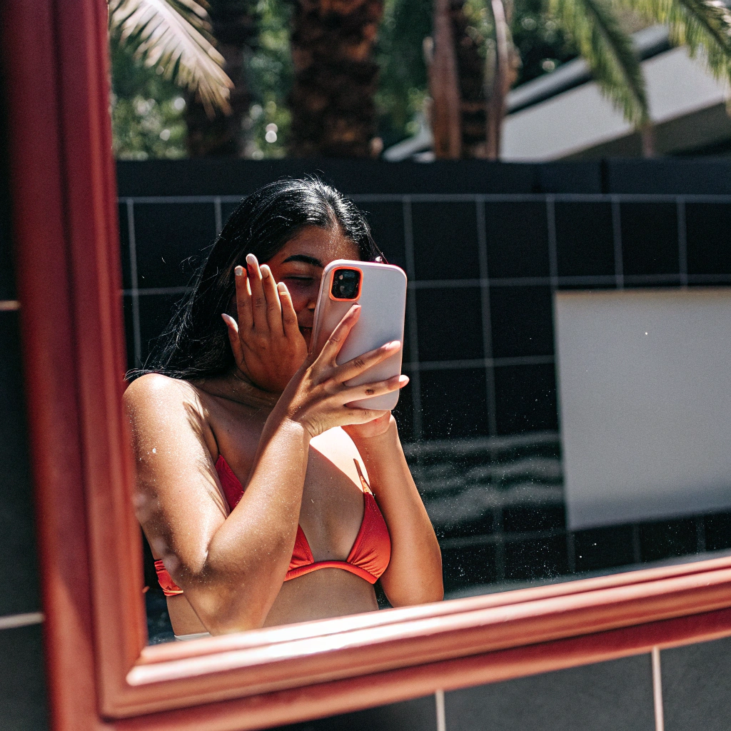 AI generated image by Red Panda AI: A thin curvy latina girl aged 23 in a bikini taking mirror selfie by the pool with an iphone hiding her face with five fingers on hand 