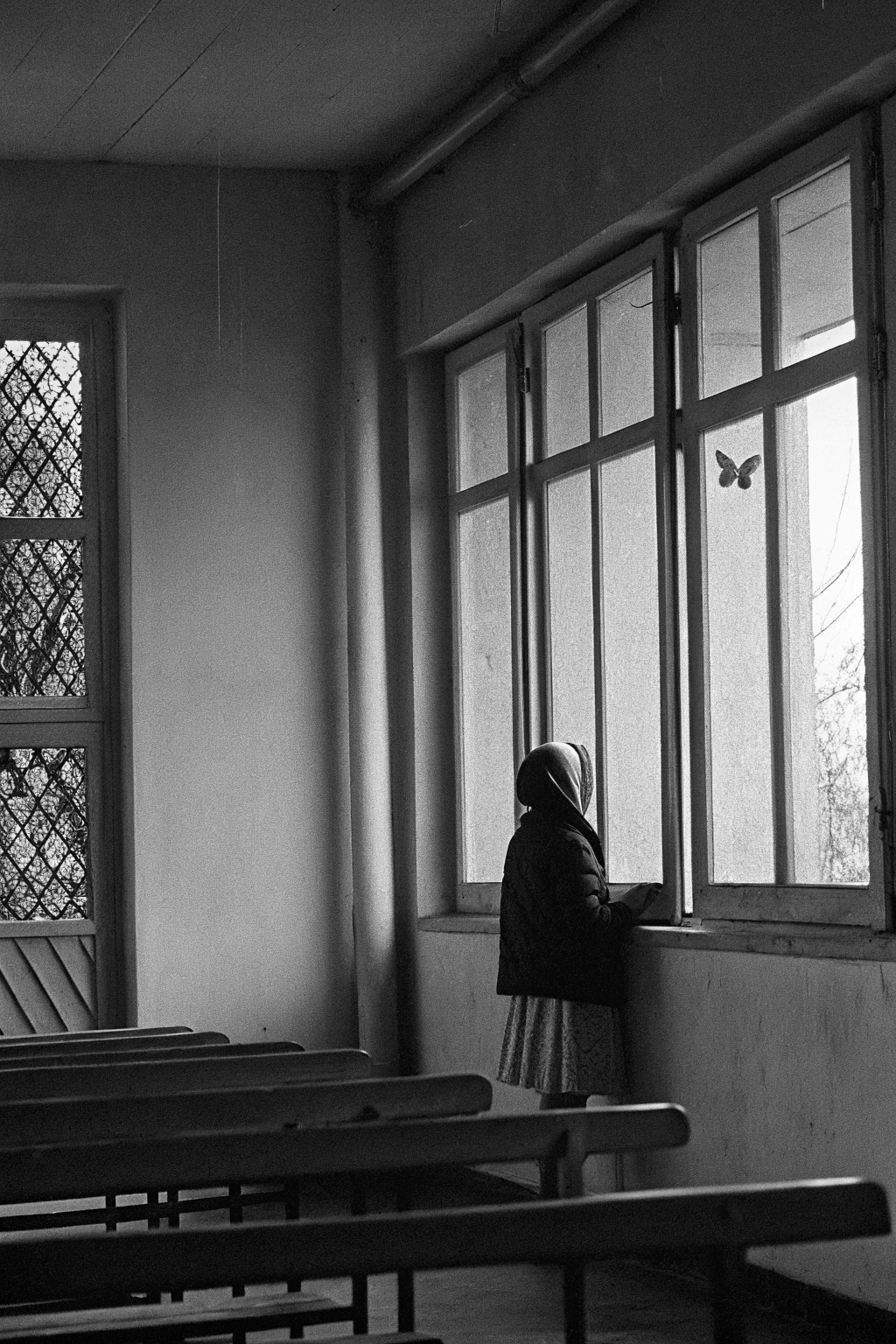 AI generated image by Red Panda AI: une photo dans le style de Robert Doisneau. Une fille à l'école élémentaire. Elle est de dos, au coin dans la la classe. Elle est punie avec un bonnet d'âne sur la tête. Elle est seule dans la classe. Un papillon se promène près d'elle.