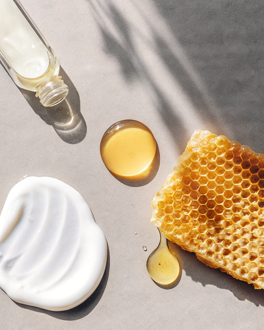 AI generated image by Red Panda AI: A minimalistic and artistic flat lay featuring natural skincare ingredients. Include a dollop of whipped tallow, a clear oil droplet, a smear of golden honey, a small puddle of amber-colored oil, and a drop of light yellow to pale amber-colored oil. Arrange these elements elegantly on a soft beige background. Use soft lighting to highlight textures and transparency, creating a clean, luxurious, and natural aesthetic.