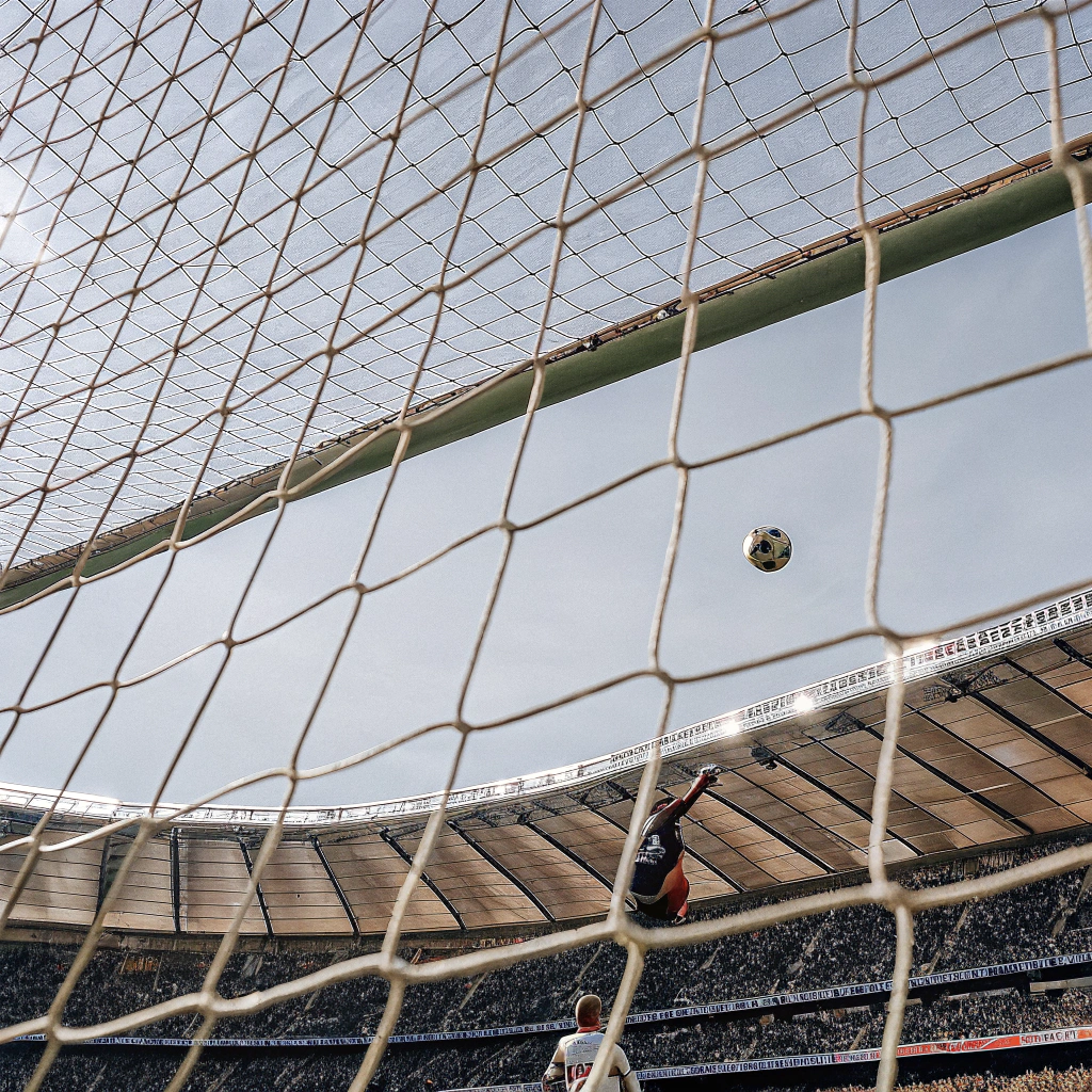 AI generated image by Red Panda AI: A football player from FC Barcelona scoring a goal to Real Madrid in a new and full Camp Nou Stadium plenty of cheering people. The image is taken 40 cm above the grass and displays perfectly the player in the action, the ball flying into the goal and the goal keeper trying to stop it