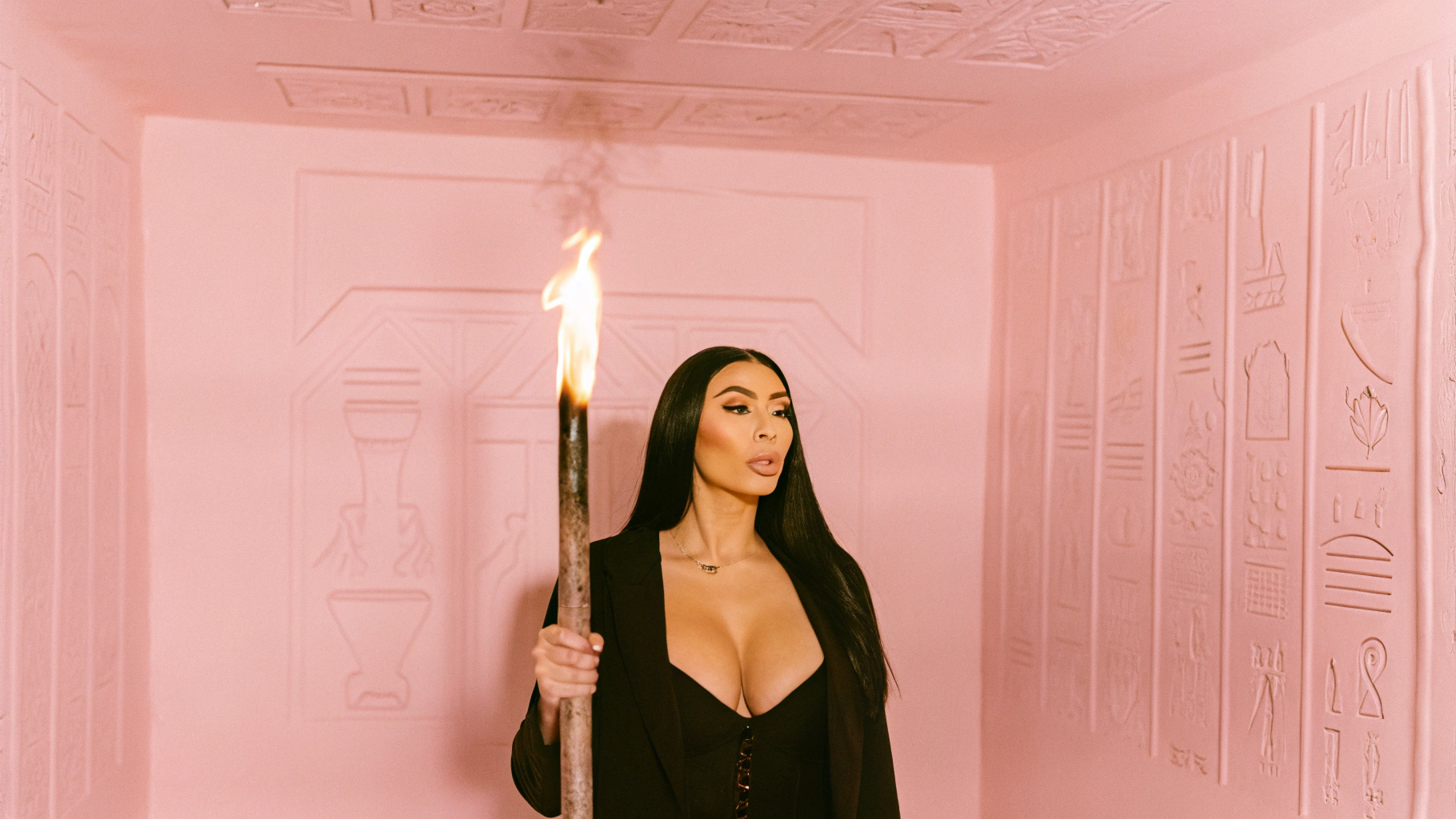 AI generated image by Red Panda AI: Generate an image of a woman standing in an ancient Egyptian tomb, holding a burning torch. The woman must have long, dark hair and be dressed in dark, elegant clothing, with a low neckline that allows her full breasts to be seen. The tomb walls are said to be adorned with intricate hieroglyphics and ancient Egyptian art. The lighting should be dim and shadowy, with the torch being the main source of light, casting dramatic shadows on the walls and the woman's face.