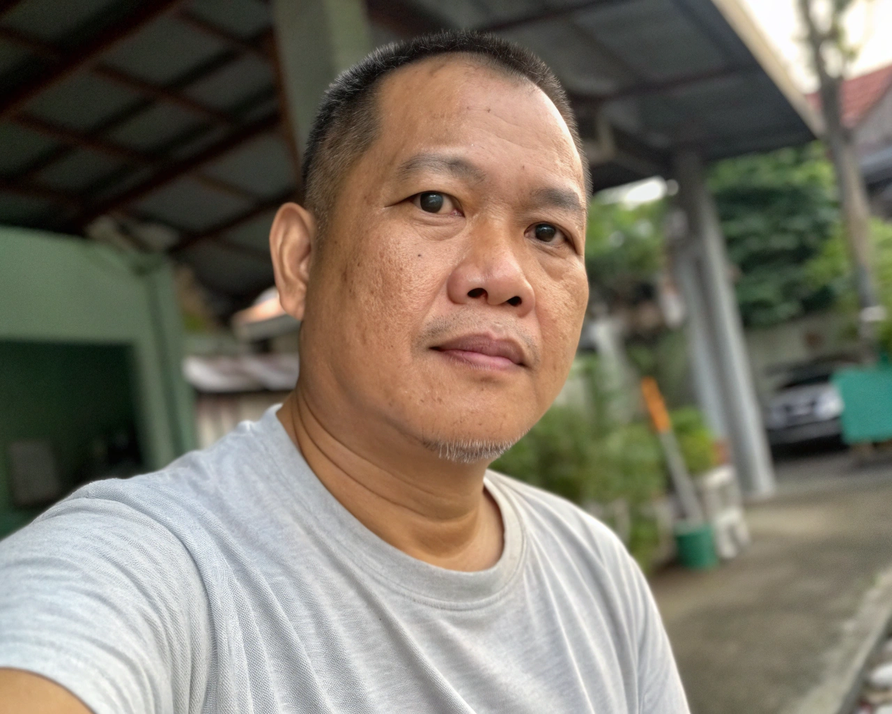 AI generated image by Red Panda AI: selfie portrait taken on iphone. thai middle-aged man, neutral expression, looking straight at the camera, ears clearly visible, short hair, bright sclera, clear black eyes, semi-blurry, phone shot of low quality, tshirt