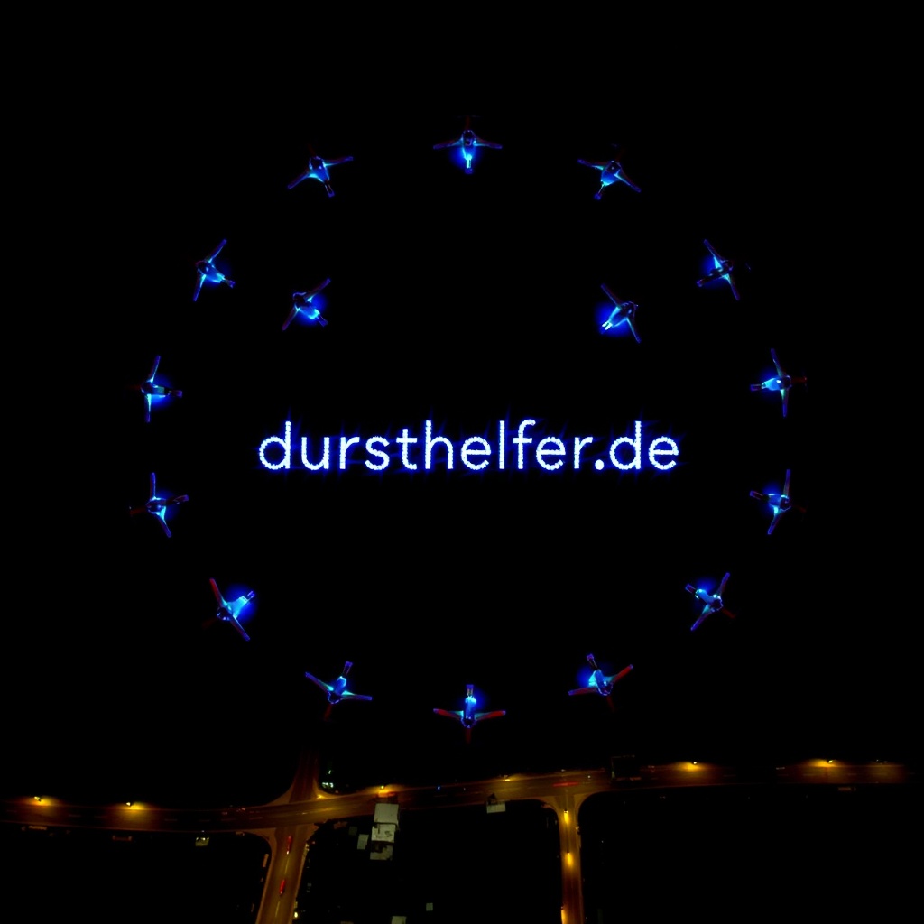AI generated image by FLUX.1-schnell: An aerial night scene with a formation of drones lighting up in a large circular pattern, spelling out 'dursthelfer.de' in the center. The drones are arranged to create a cohesive design, using vibrant blue lights with some complementary colors to add detail. The design has a futuristic look, with additional simple shapes or lines around the text, similar to a digital display. The city lights below add depth, making the drones' lights stand out against the dark sky.
