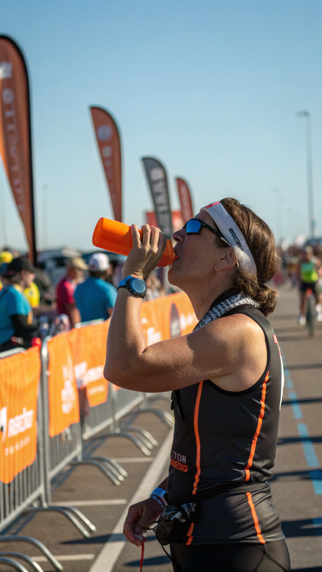 AI generated image by Red Panda AI: adulto triatleta, en un día de sol, en un puesto de avituallamiento, bebiendo agua de un vaso plástico color naranja, durante el pedestrismo. el puesto de avituallamiento se ve, y viene vanderas color naranja