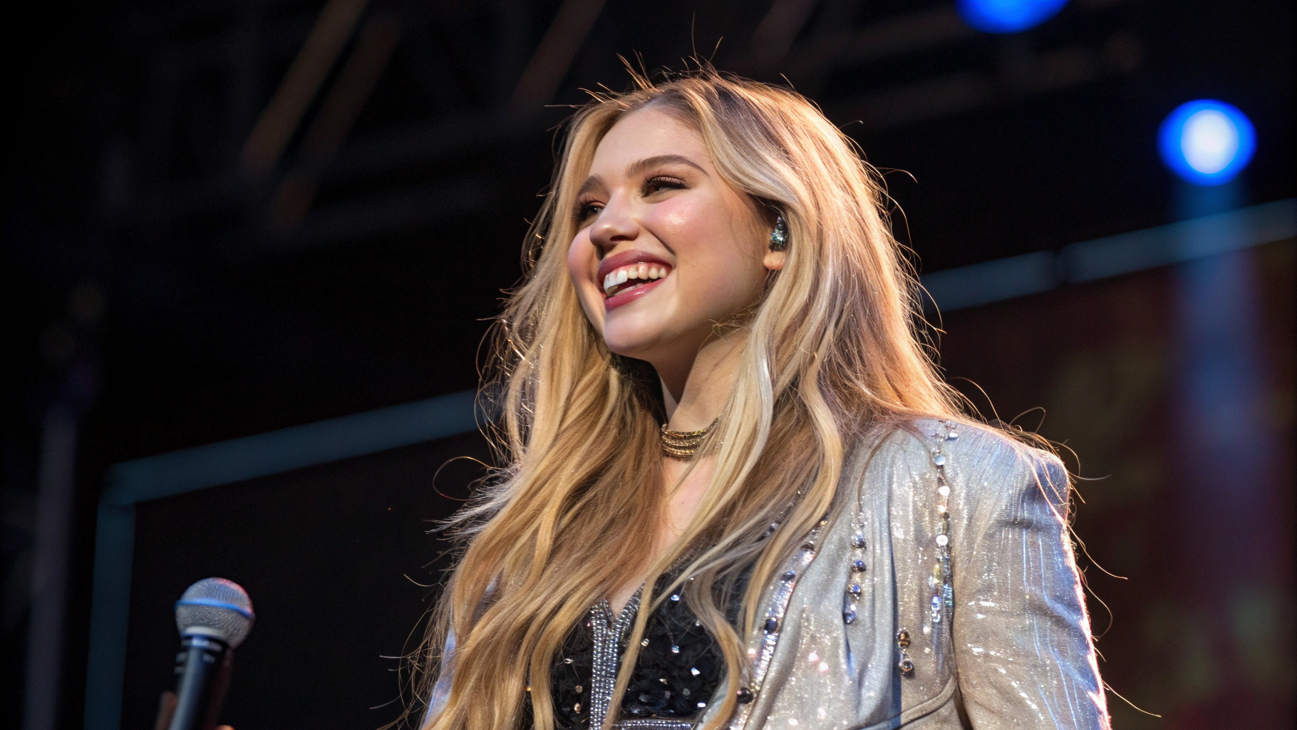 AI generated image by Red Panda AI: une jeune femme blonde chanteuse, avec des cheveux long, souriante, dans une tenue de scène