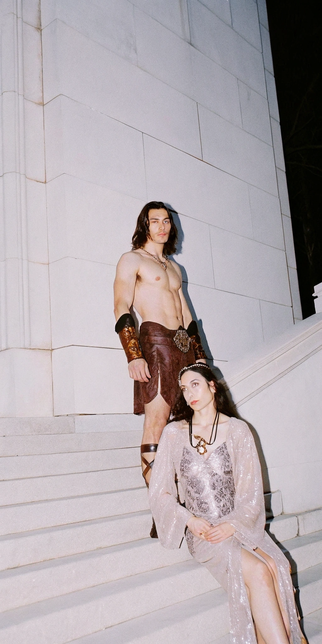 AI generated image by Recraft V3: heroic fantasy scene, massive stone palace steps, cinematic shot of a muscular barbarian warrior and ethereal sorceress on ancient stone steps, shirtless warrior wearing leather bracers and bronze medallion, weathered face, long dark hair, glistening muscles, rugged brown leather pants, stoic expression || mystical woman in translucent flowing robe with intricate silver embroidery and sparkling details, hooded veil, pale skin, dark straight hair, ornate jewelry, seductive pose, ethereal beauty || grand marble staircase, greco-roman architecture, dramatic side lighting, moody atmosphere, deep shadows, warm highlights, epic fantasy aesthetic, 1980s practical effects, film grain, anamorphic lens, Kodak motion picture film, golden hour lighting, high production value, ultra detailed, photorealistic, high contrast, dramatic composition --ar 16:9 --style raw --cinematography by John Alcott