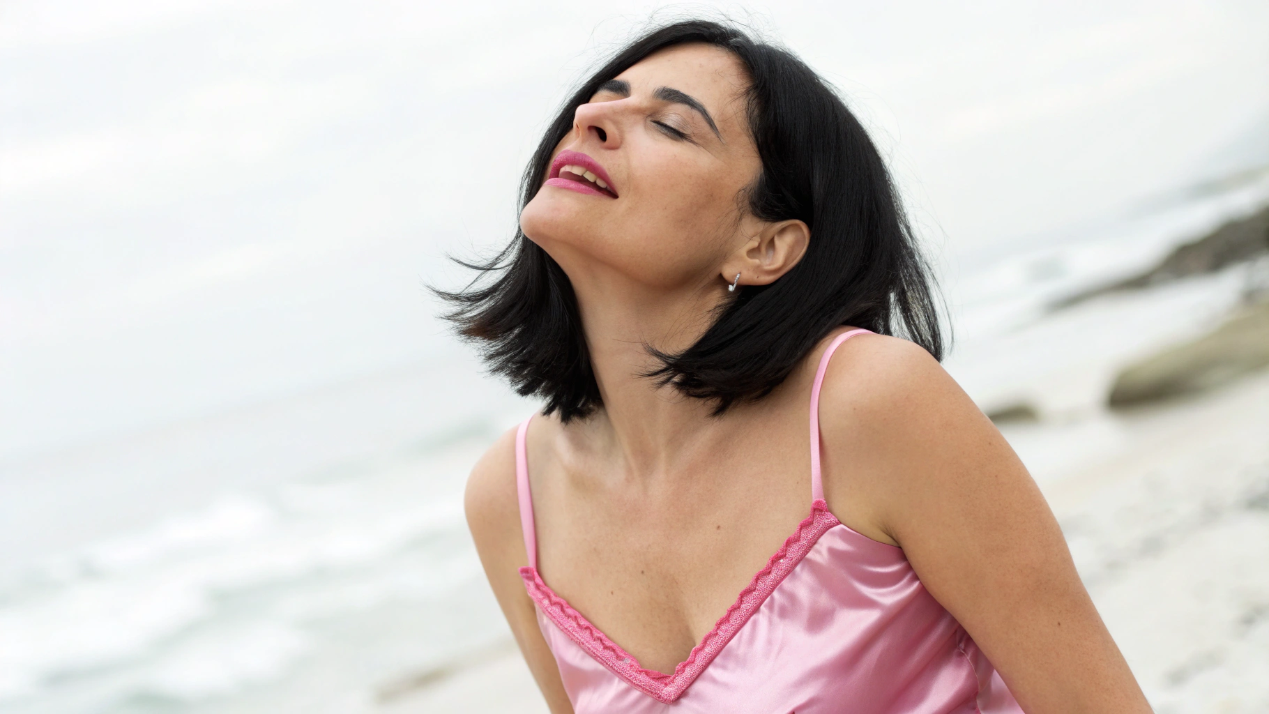 AI generated image by Red Panda AI: A beautiuful image of a 38 year old white latin woman with black medium long hair dressed in a pink satin spaghetti strap pijama, with her face tilted up, eyes closed and mouth slightly open with a facial expression of gratification