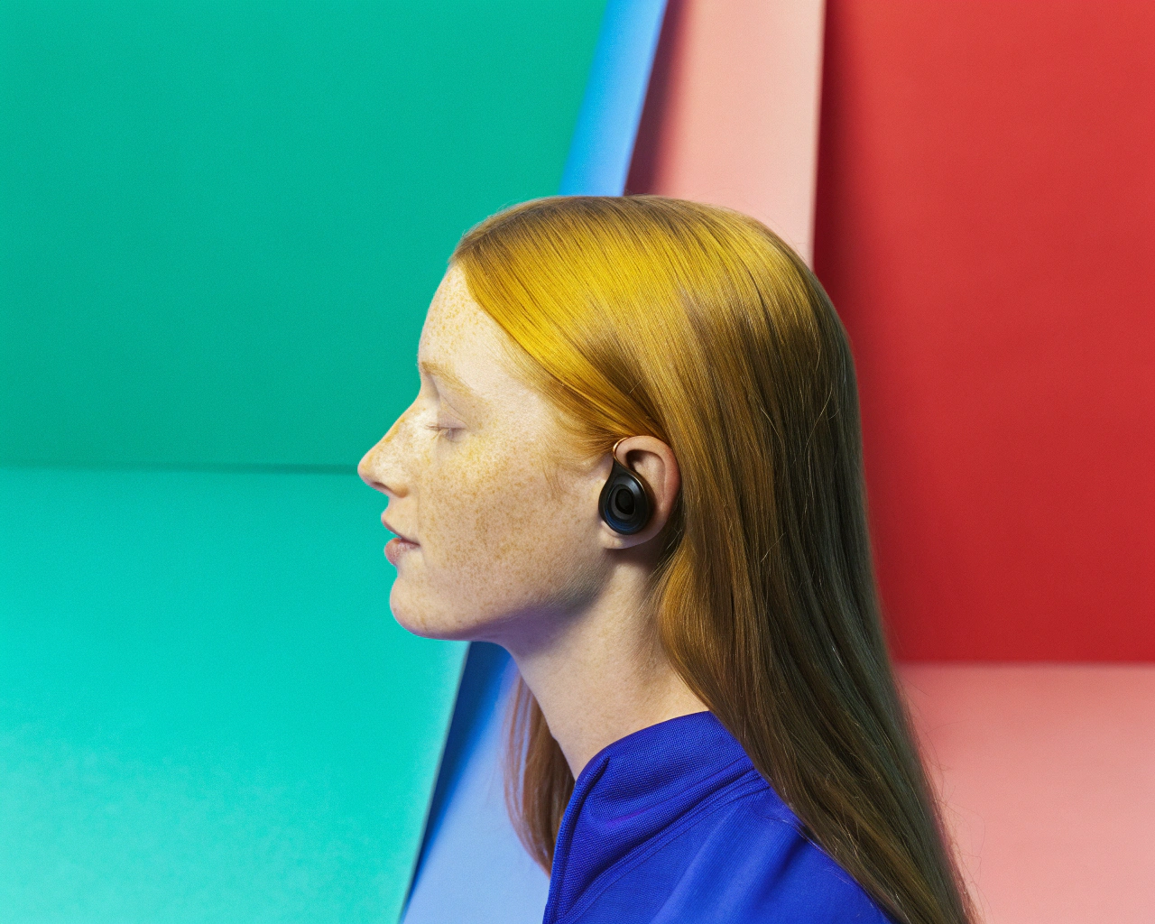 AI generated image by Red Panda AI: Realistic portrait in half profile, of a beautiful young redhead, milky white skin, very smooth, a few freckles, straight hair down to her shoulders. Long and thin neck. Her ears uncovered, with a Bluetooth headset in her ear. Background of the scene with depth of field. Warm colors. Neutral and minimalist background.